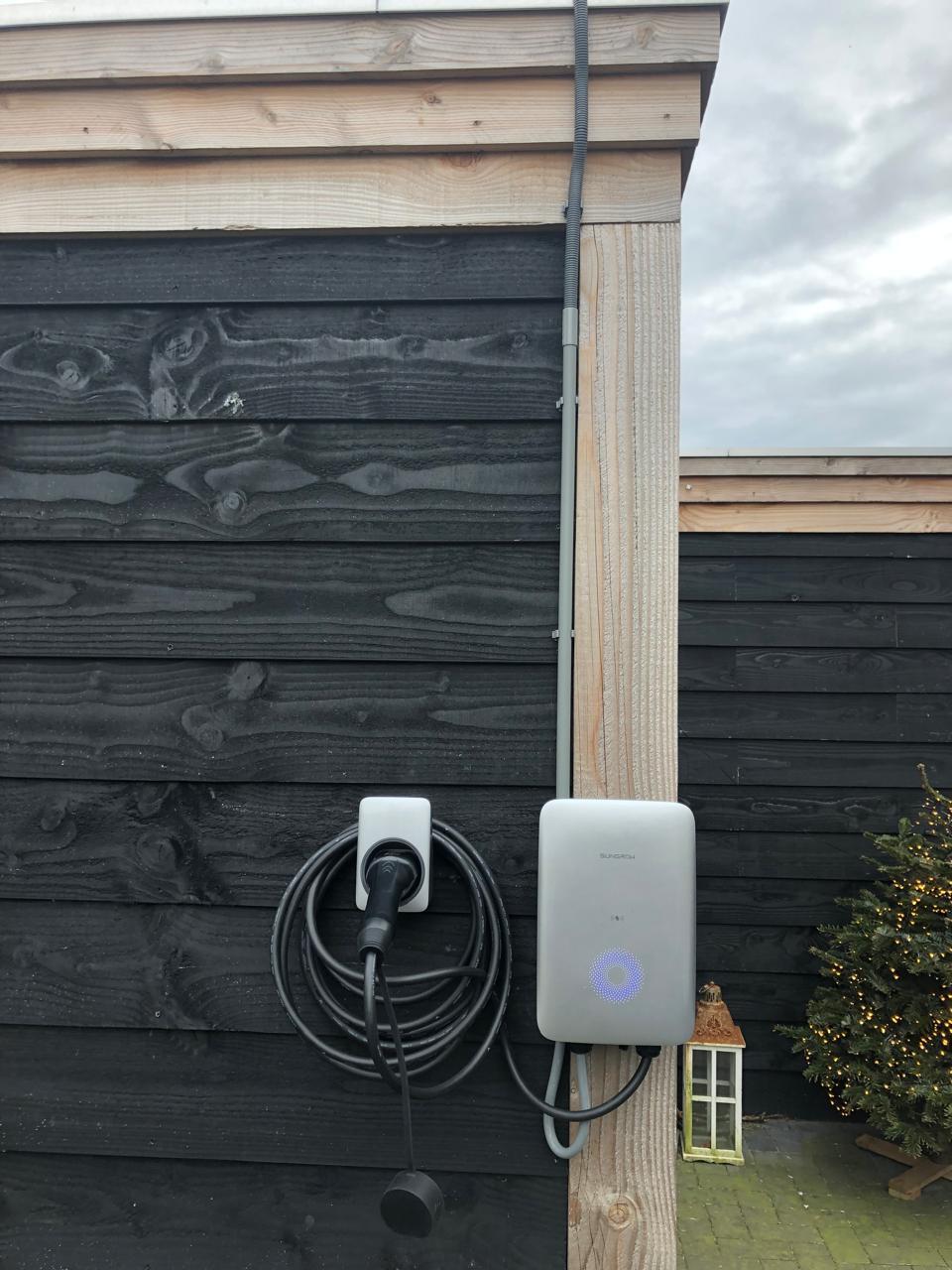 Door GS Solar geïnstalleerd laadpunt aan een zwarte houten wand